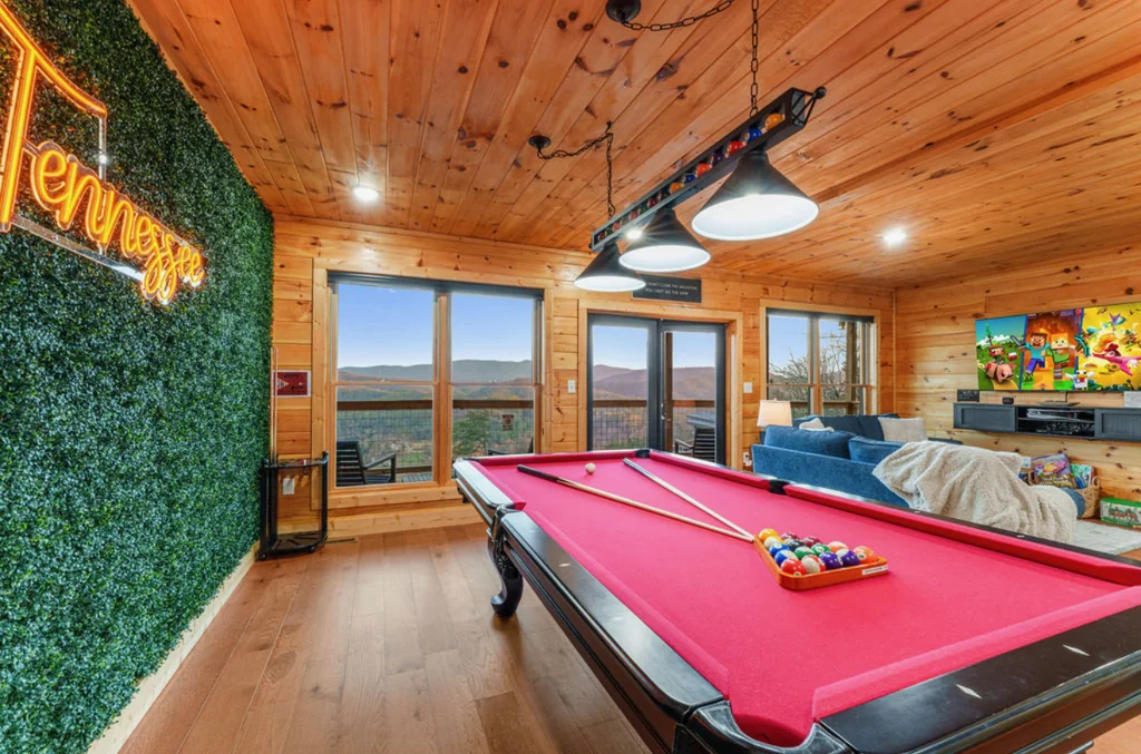Game room with a red-felt pool table, Tennessee sign, lounge seating, television, and mountain views through wide windows