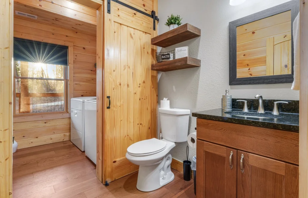 Half bath with a wood vanity, dark granite counter, framed mirror, toilet, floating shelves, and a sliding pine barn door