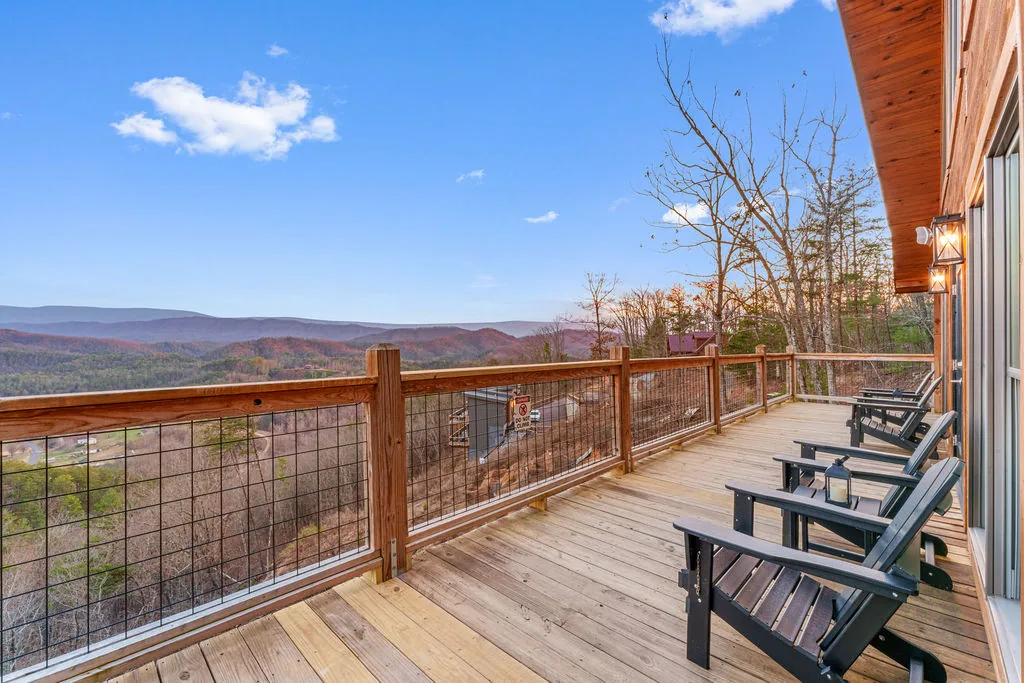 Wraparound cabin deck with Adirondack chairs overlooking the wooded valley and Smoky Mountain ridges