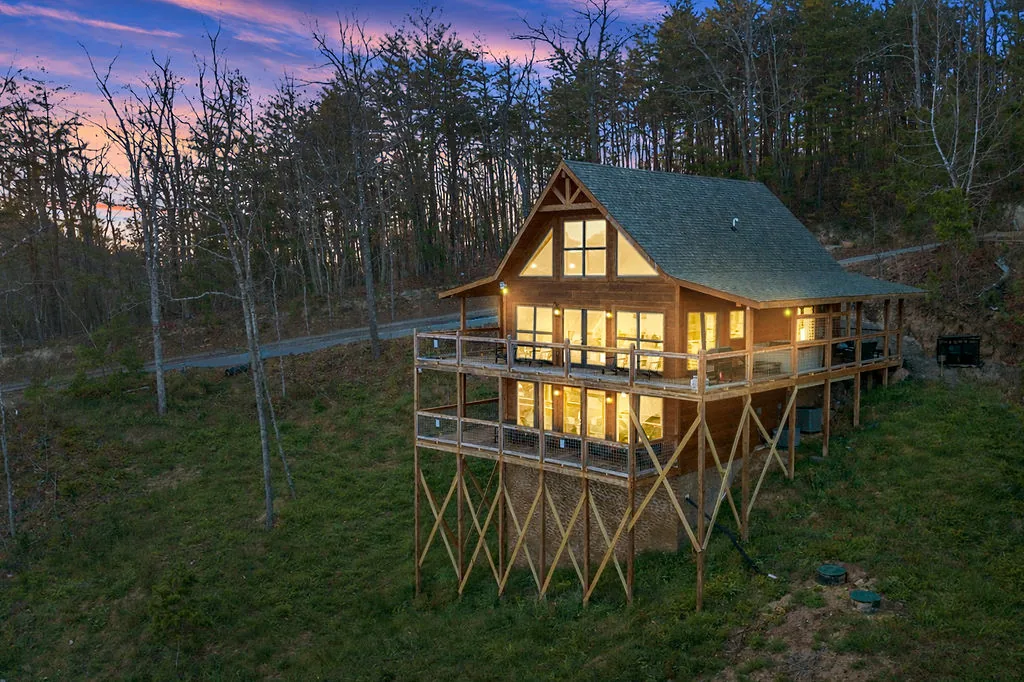 The cabin lit from within at twilight with a pink and blue sky behind the ridge