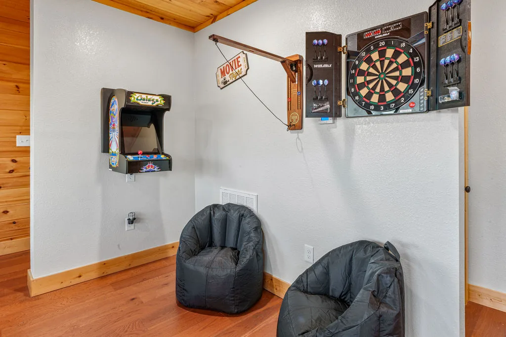 Dart board and arcade cabinet in the corner of the game room with bean bag chairs