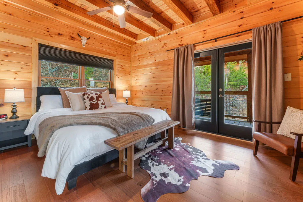 King bed with layered linens and a cowhide rug beside French doors to the deck
