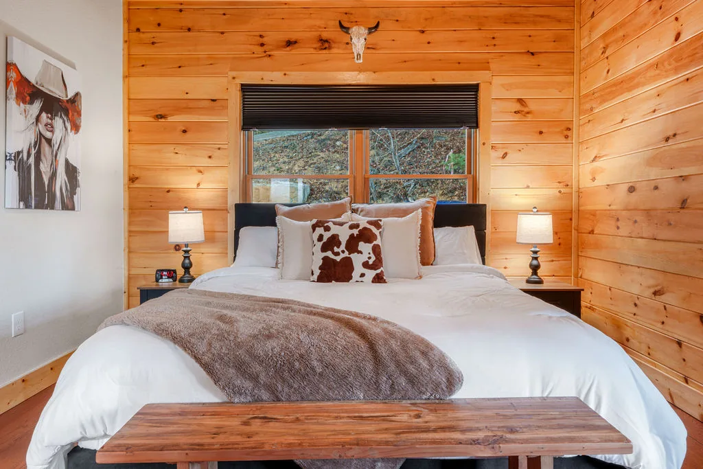 King bedroom with a wood-framed bed, bench at the foot, and pine plank walls
